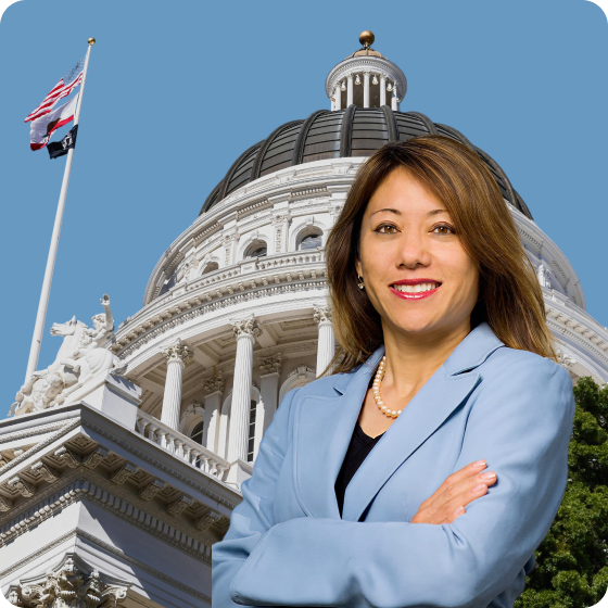 A woman standing confidently in front of the California State Capitol building. The building features a large dome, tall white columns, and the California state flag flying beside it.