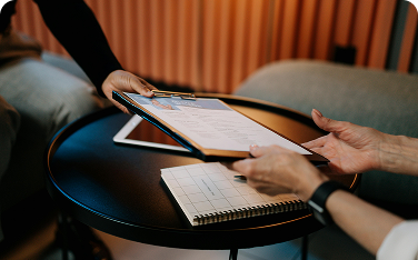 Close-up of two people's hands passing a clipboard with a document (likely a resume or application) over a small, round black table.